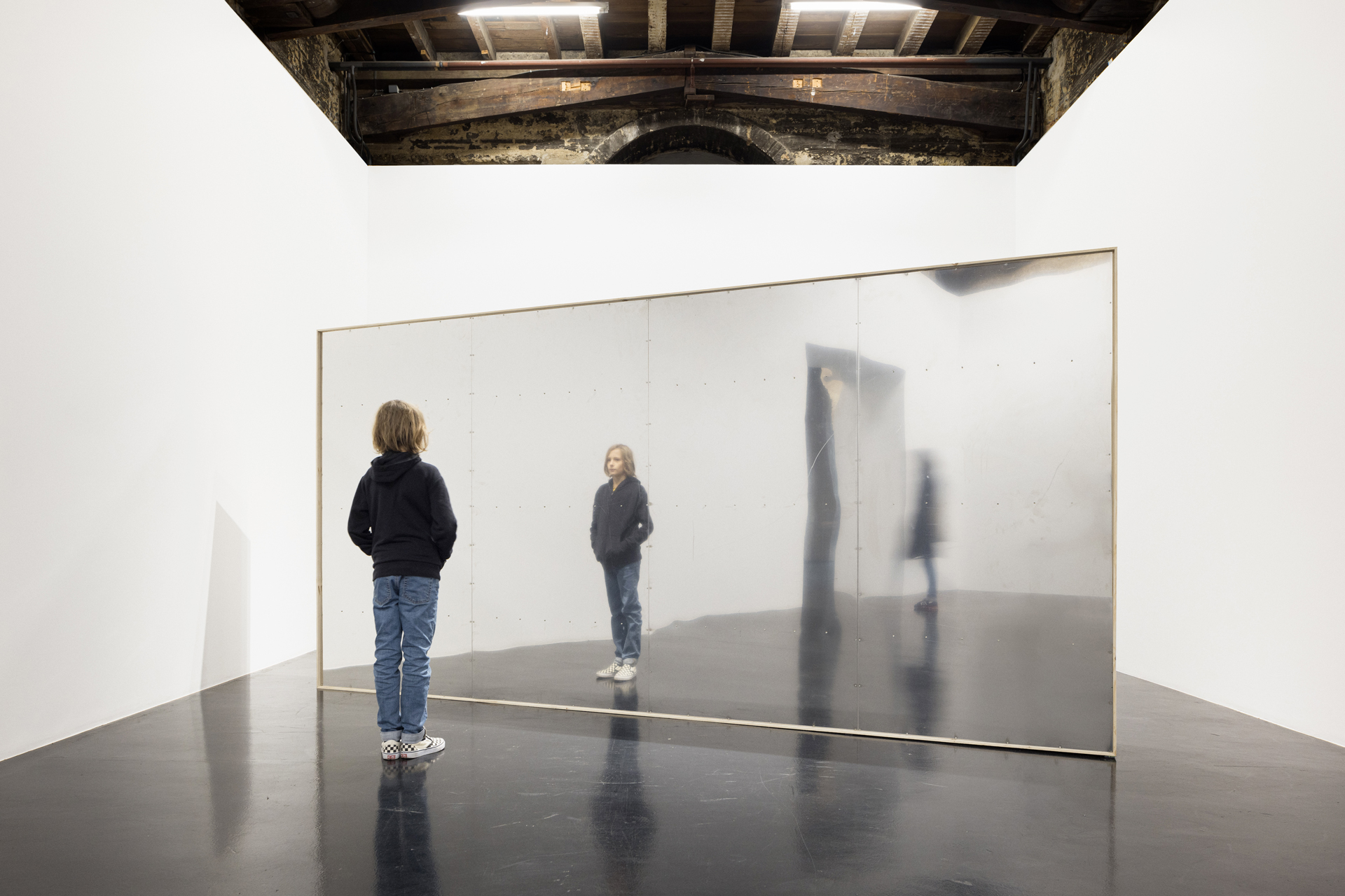 Un adolescent seul dans un espace d'exposition regarde son reflet dans un miroir