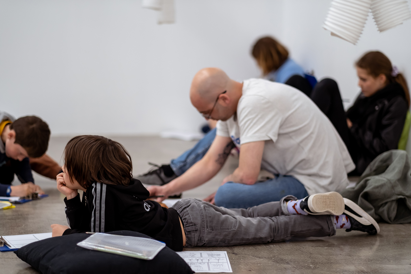 Des adultes et des enfants assis dans un espace d'exposition sont en train de dessiner