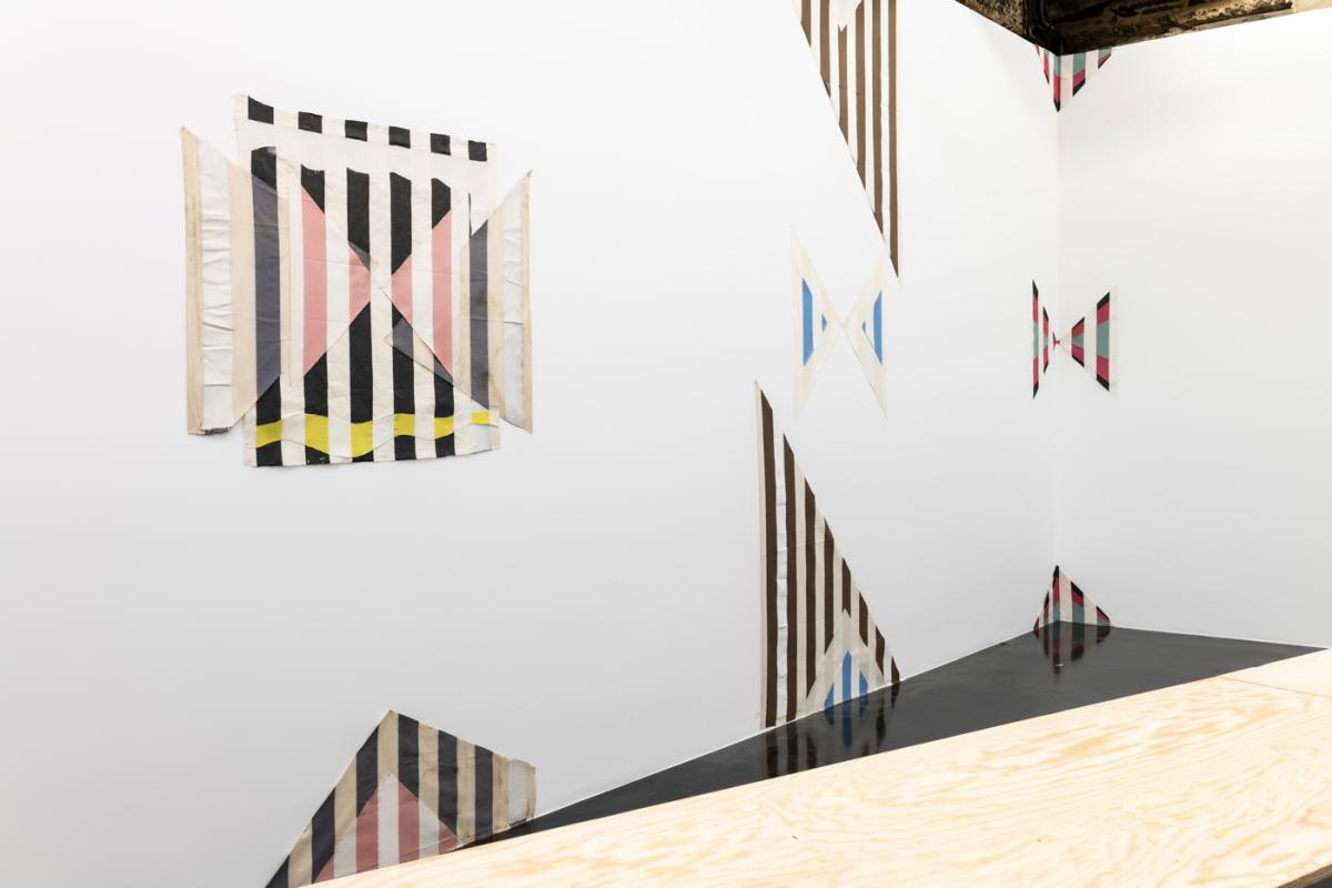 Sur un mur blanc, des peintures géométriques brunes, bleues et roses, découpées selon des bandes toutes de la même largeur