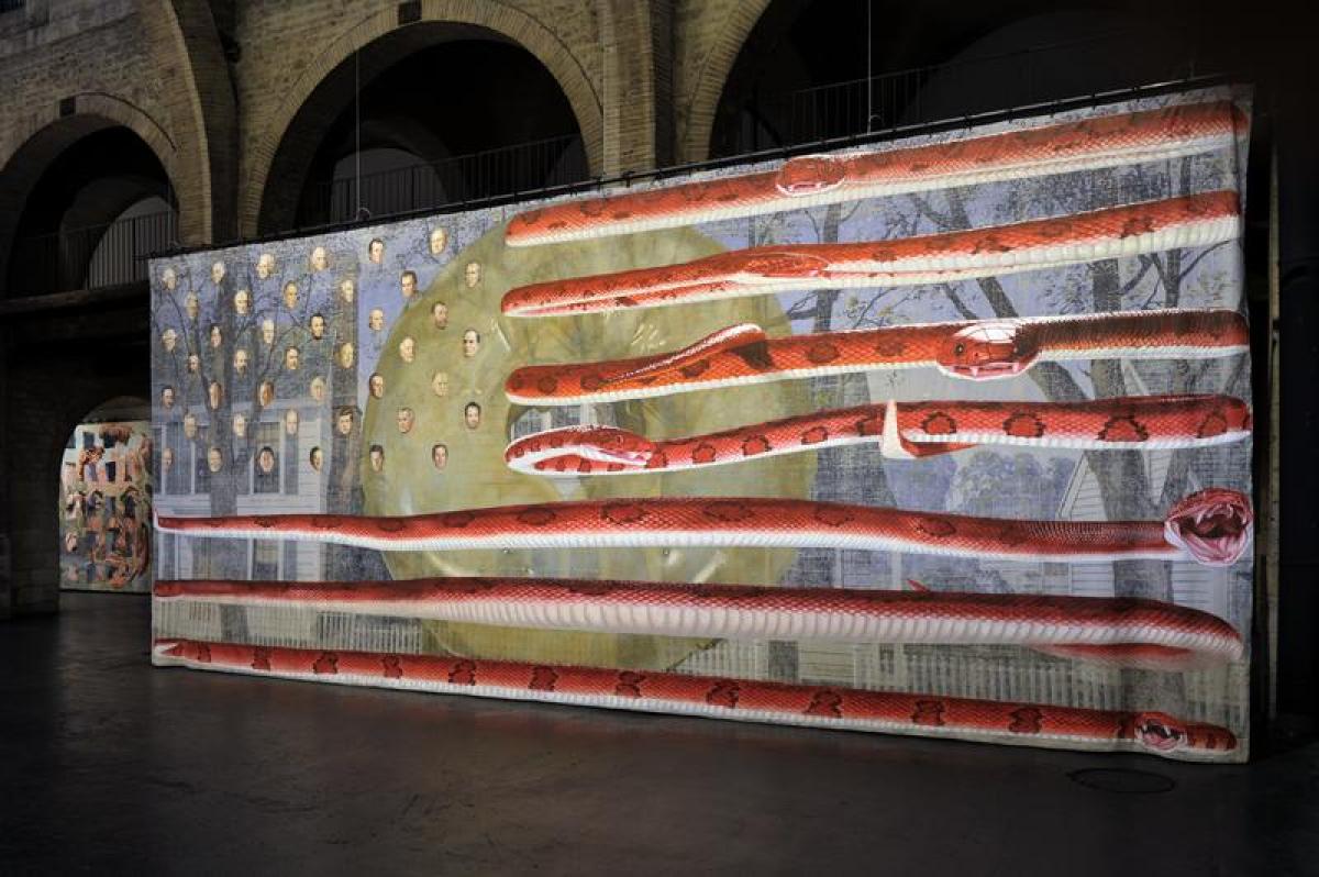 Sur une toile monumentale, comme le drapeaux américain, dont les étoiles sont remplacées par les visages des présidents américains et les lignes sont remplacées par des serpents rouges