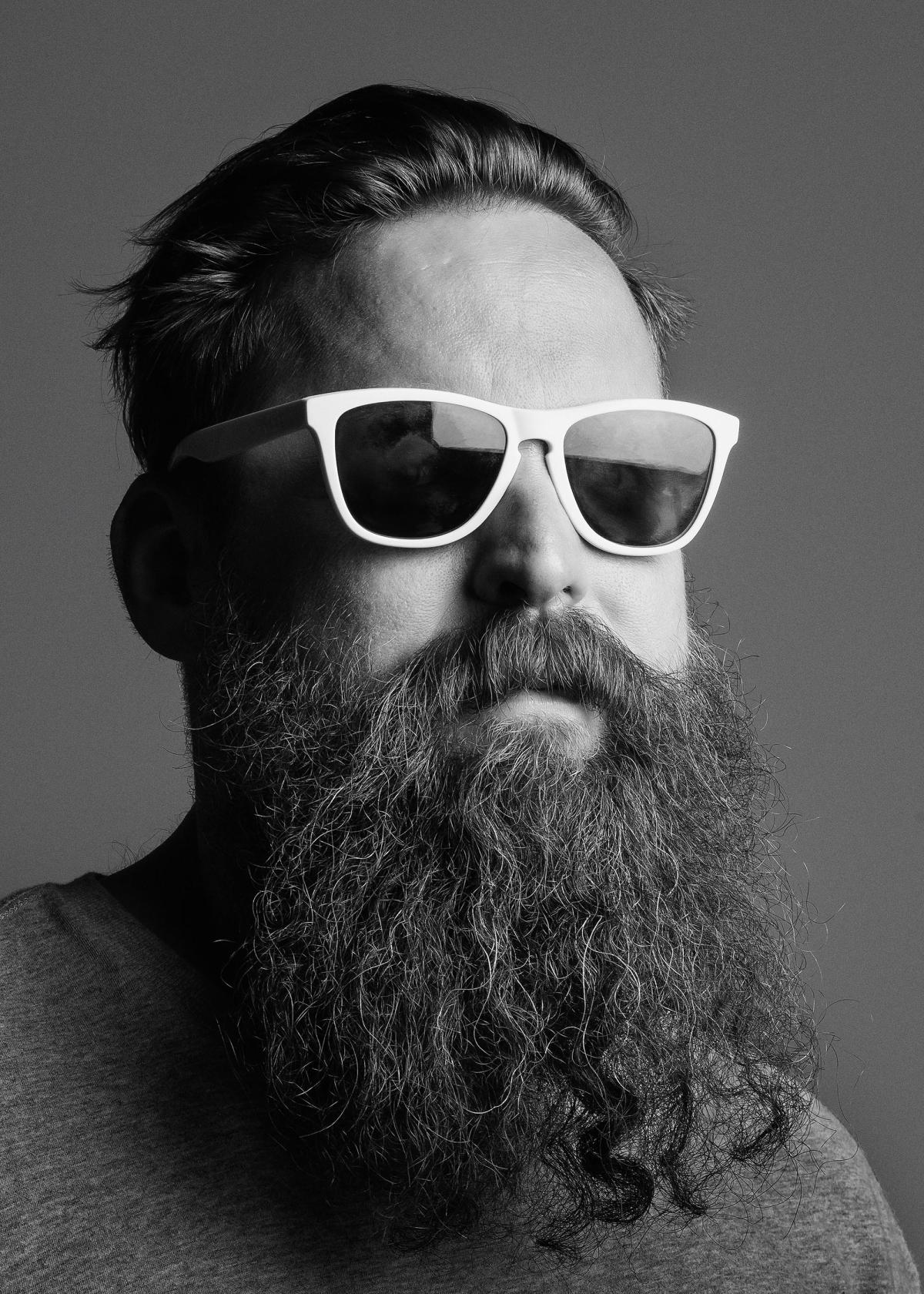 Portrait d'Aaron Curry en noir et blanc avec des lunettes de soleil et une longue barbe 