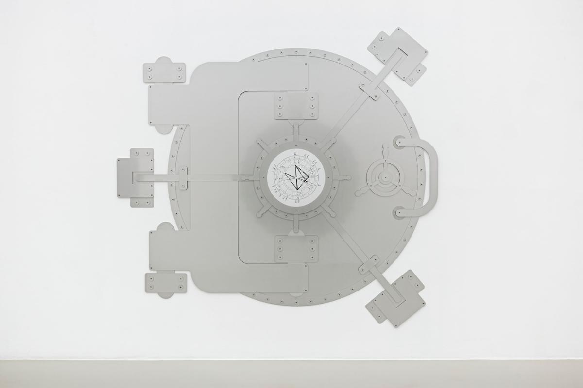 Sur un mur blanc, la reproduction plane, en métal, d'une grande porte "blindée" ronde et de grande dimension, avec de nombreux systèmes de verrouillage.